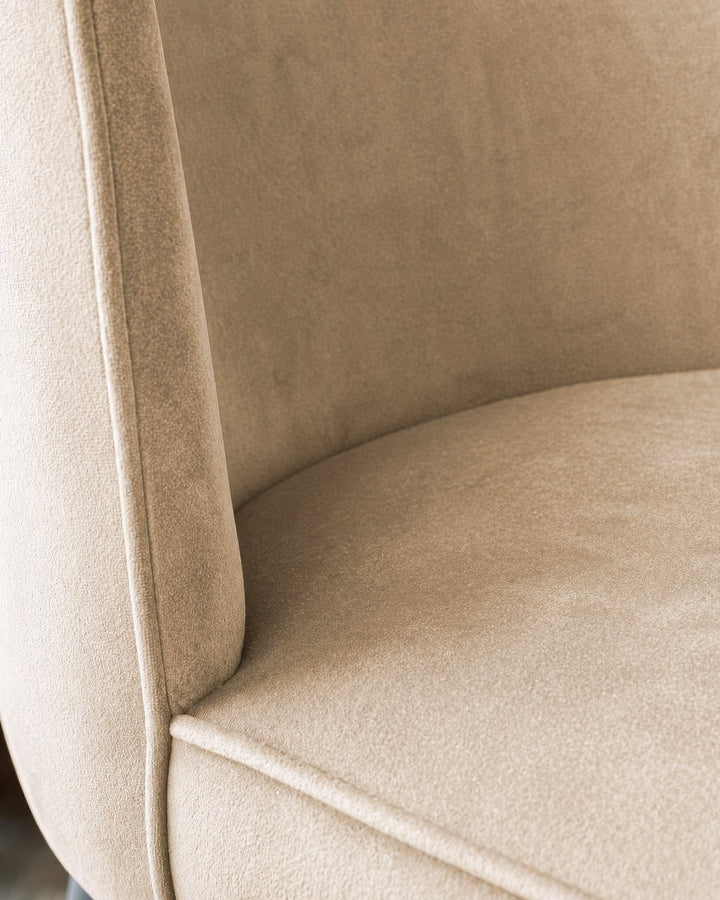 Champagne velvet dining chair close-up showing curved armrest and seat cushion detail.