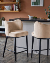 Evelyn bar stools in champagne velvet with black wooden legs, shown as a pair at a black marble countertop in a styled interior.