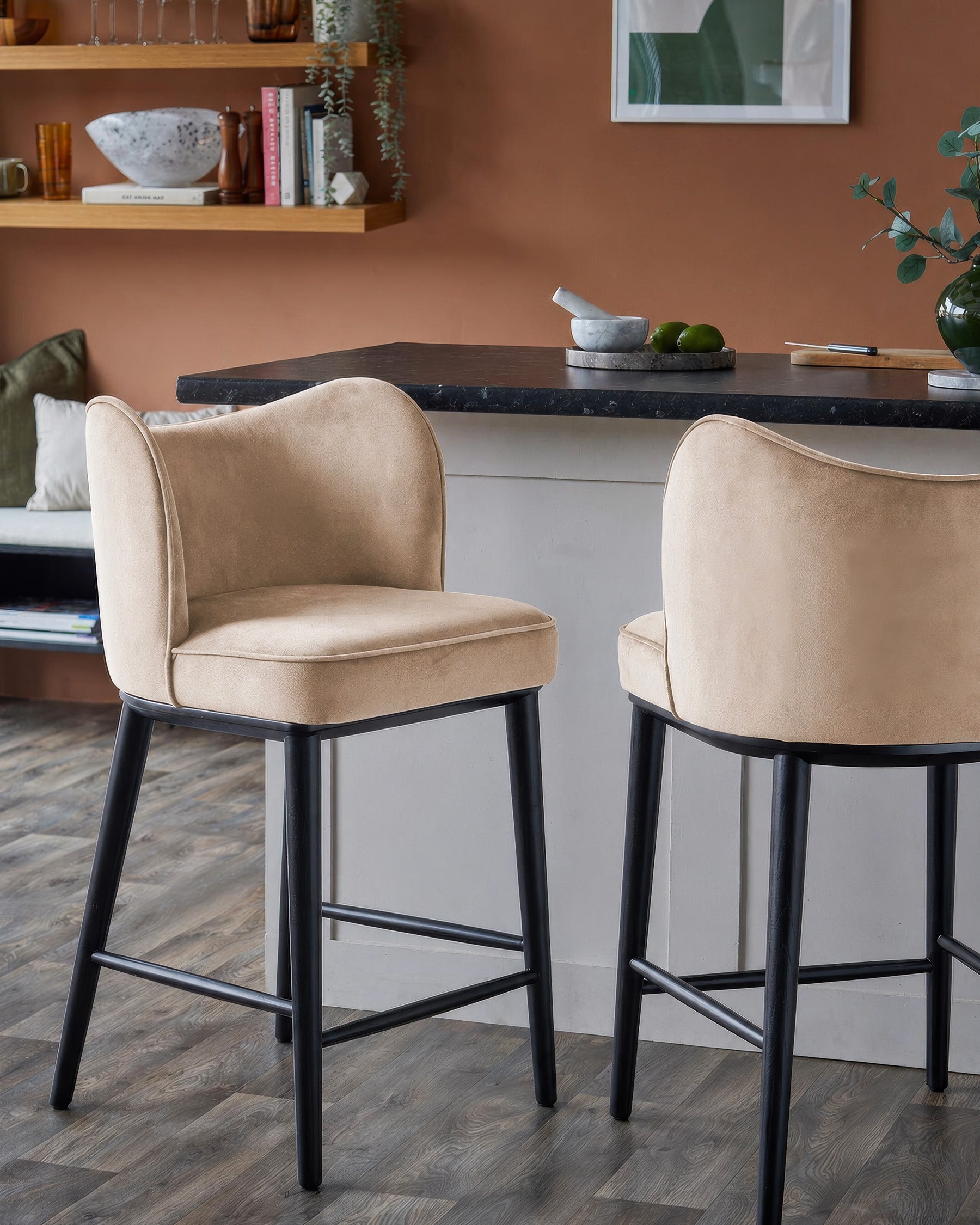 Evelyn bar stools in champagne velvet with black wooden legs, shown as a pair at a black marble countertop in a styled interior.