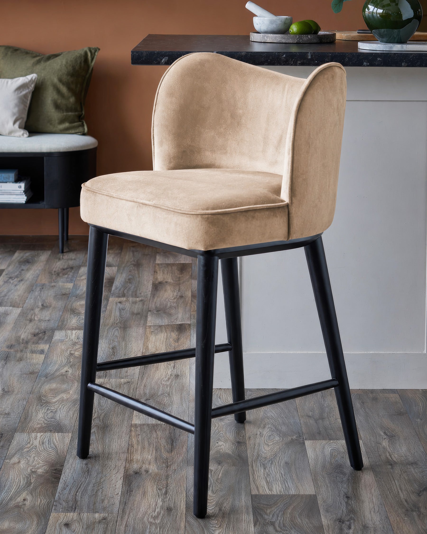 Evelyn bar stool in champagne velvet with black wooden legs, shown in a modern living room setting.