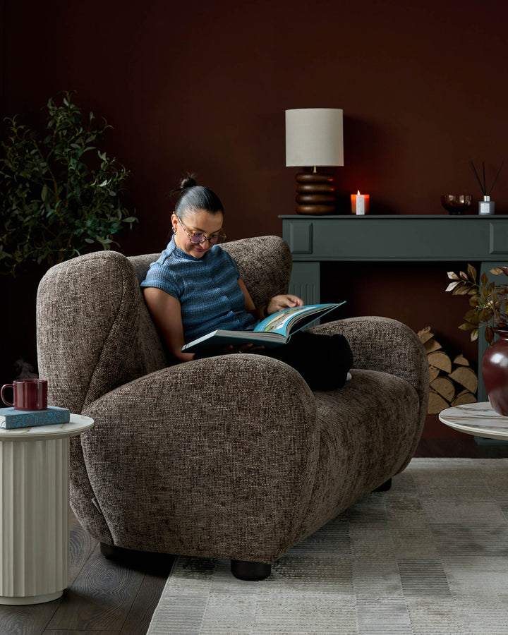 Mocha fabric two-seater sofa with curved arms and black legs, styled in a cozy living room setting.