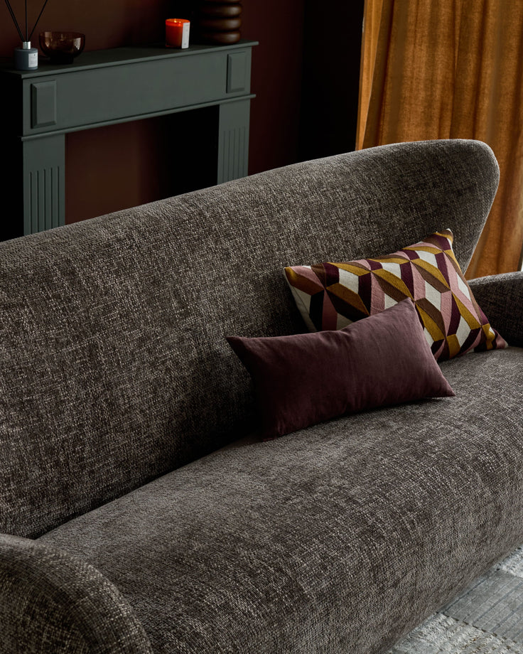 Mocha fabric two-seater sofa with rounded arms, styled with burgundy and patterned cushions in a living room setting.