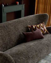 Evelyn 2-seater sofa in mocha fabric, angled view with decorative pillows, fireplace and gold curtains in background.