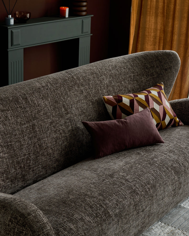 Evelyn 2-seater sofa in mocha fabric, angled view with decorative pillows, fireplace and gold curtains in background.