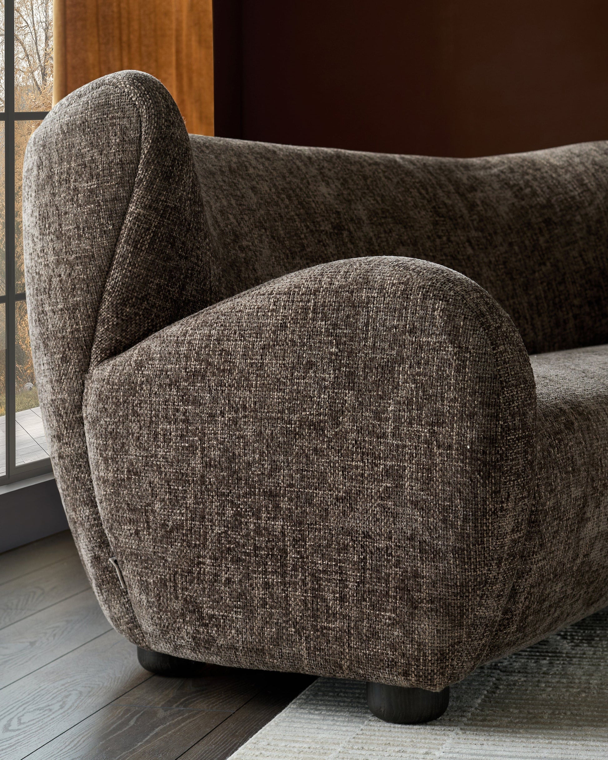 Evelyn 2-seater sofa in mocha fabric, rounded armchair style with curved backrest and dark cylindrical legs, angled side view.