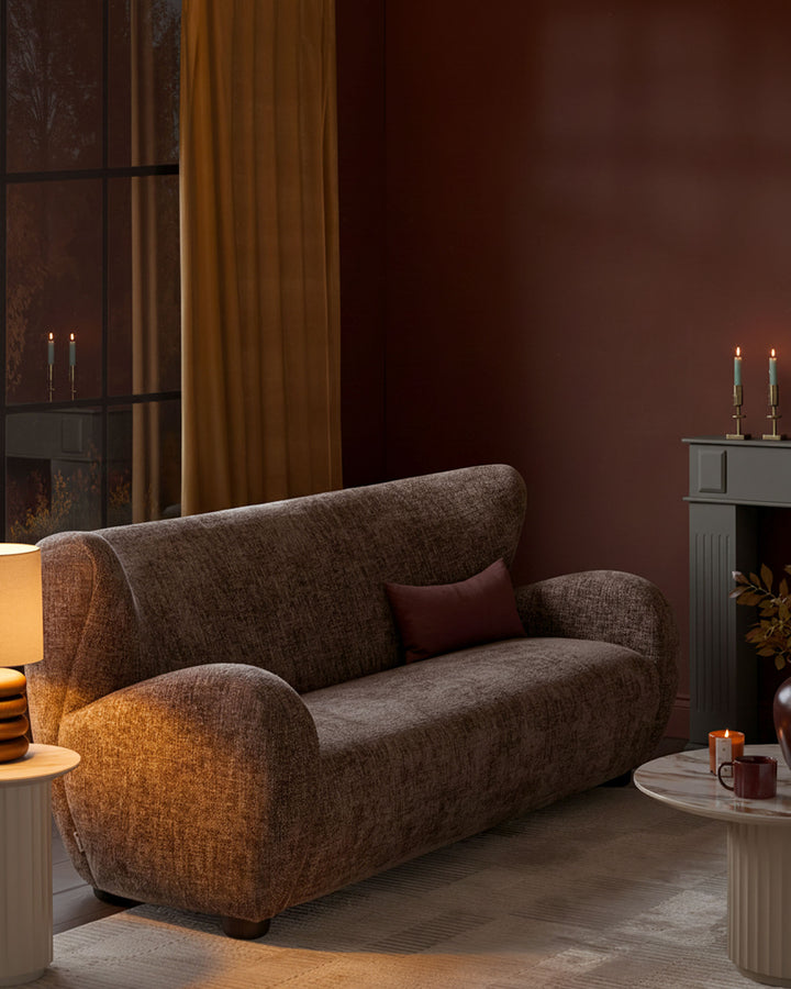 Evelyn 3-seater sofa in mocha fabric with curved arms and back, styled in a warm interior with fireplace and candles.