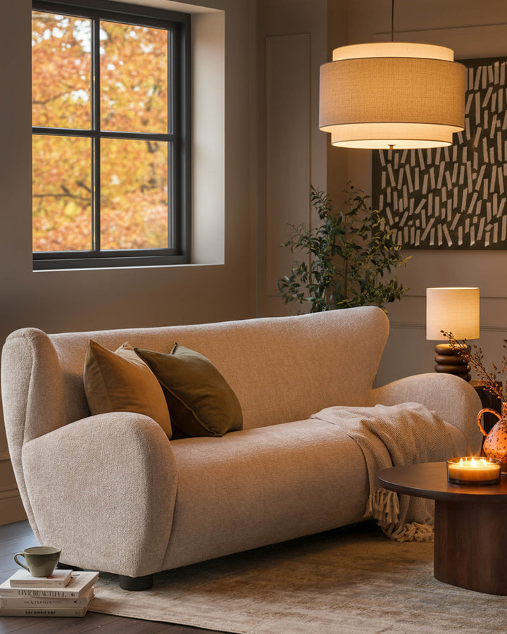 Evelyn 3-seater sofa in natural fabric with curved arms and cushions, shown in a warm autumn-themed living room setting.