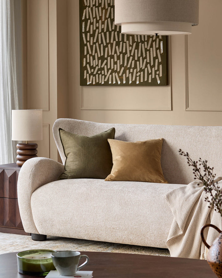 Evelyn 3-seater sofa in natural fabric with curved arms, styled with olive and tan cushions in a neutral living room.