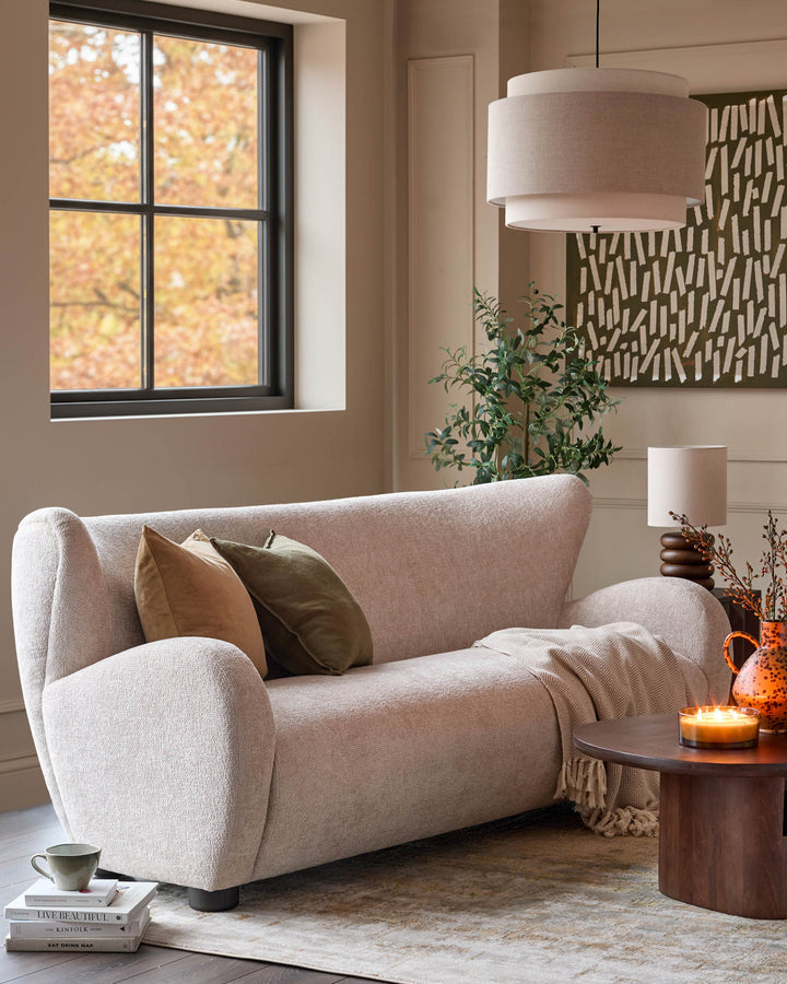 Evelyn 3-seater sofa in natural fabric with curved arms, displayed in a warm-toned living room setting.
