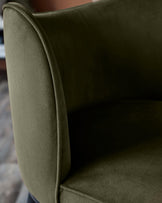 Close-up of a stylish armchair in olive green velvet, showcasing its soft texture and elegant design.