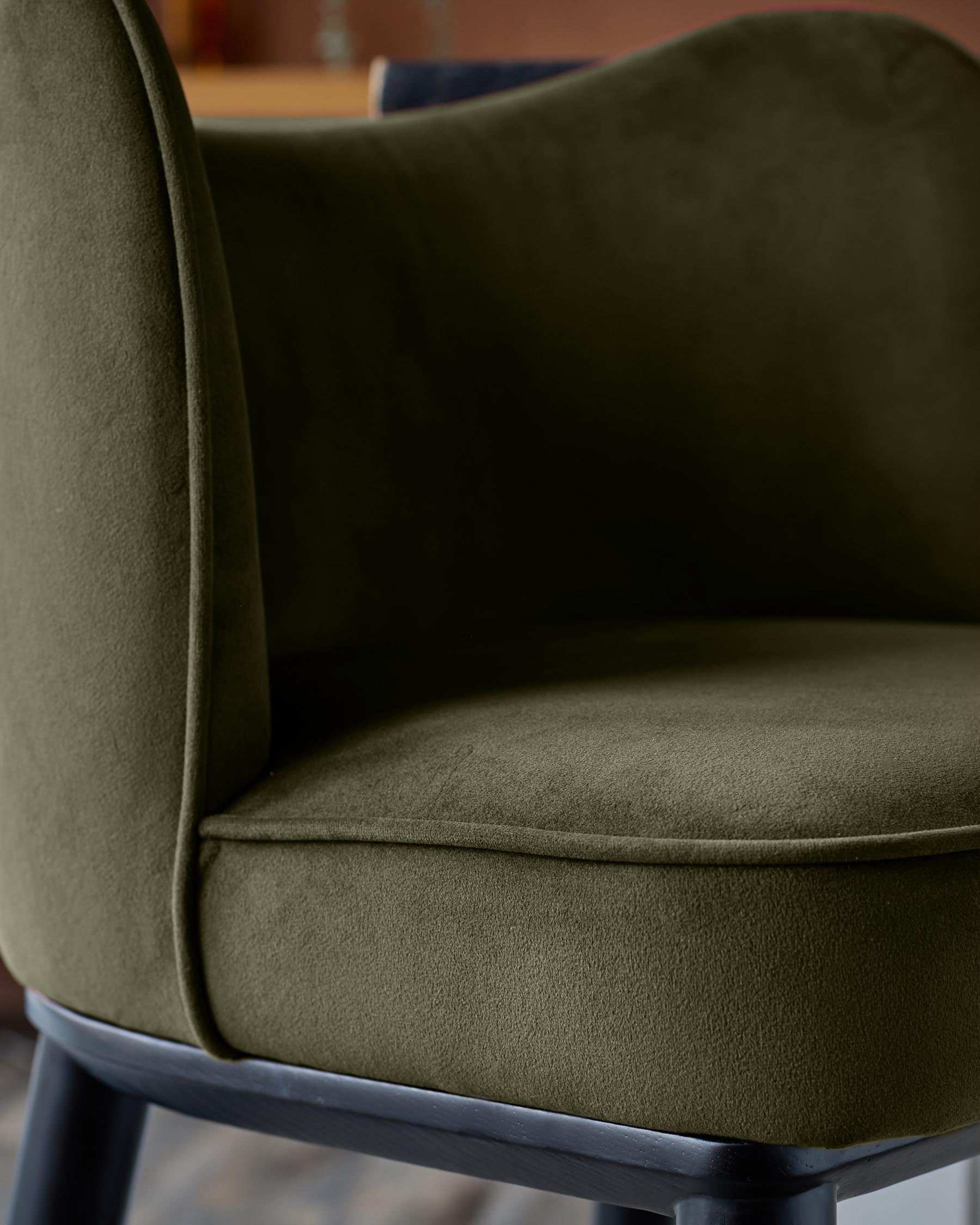 Close-up of an olive green velvet chair with a black frame, showcasing its texture and elegant design.