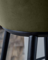 Close-up of a stool with a textured olive green seat and dark wooden legs. Modern design furniture.