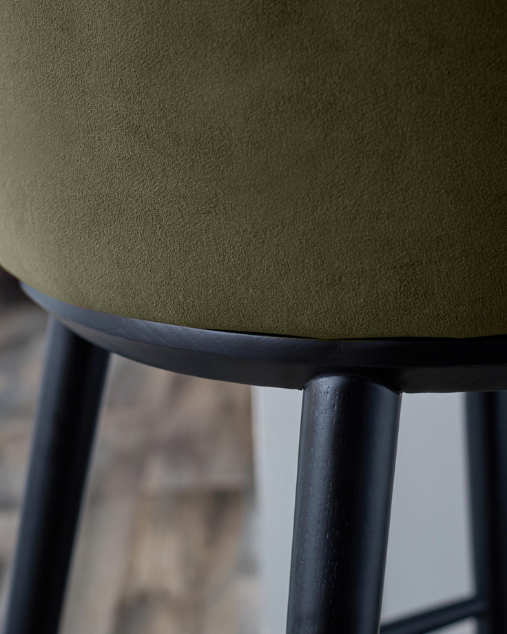 Close-up of a stool with a textured olive green seat and dark wooden legs. Modern design furniture.