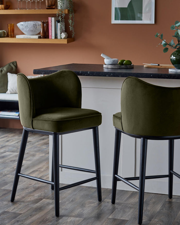 Two stylish olive green bar stools with black legs, sit under a kitchen counter in a modern kitchen.