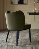 Olive green dining chair with black legs, part of a dark wood table visible. Modern design, premium feel.