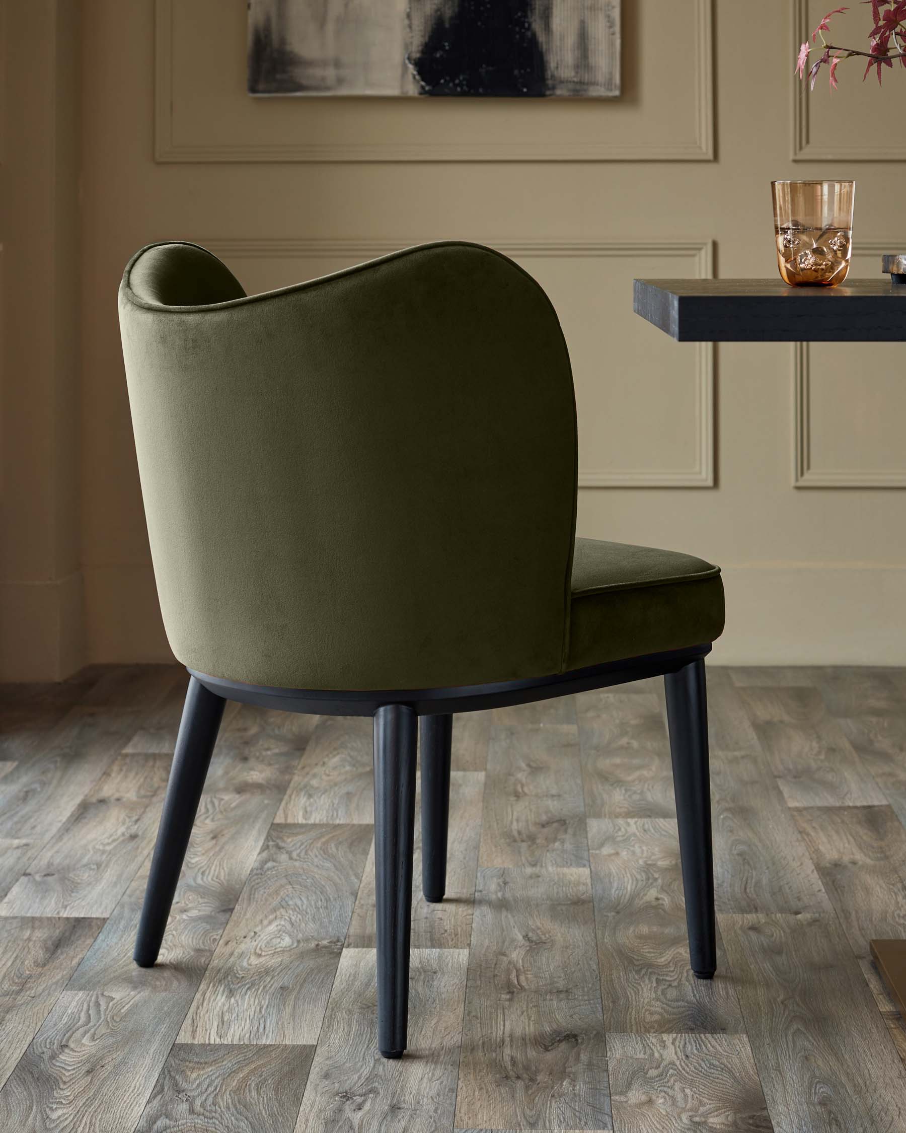 Olive green dining chair with black legs, part of a dark wood table visible. Modern design, premium feel.