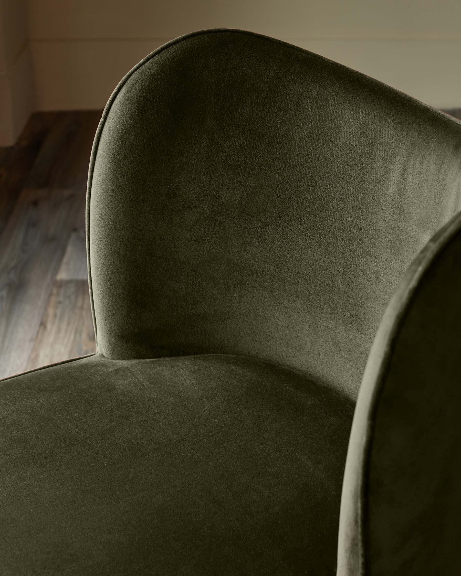Close-up of a plush, dark olive velvet armchair, showcasing its rounded back and soft texture. Elegant and inviting design.