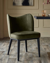 A stylish olive velvet dining chair with dark, angled legs, set against a neutral backdrop.