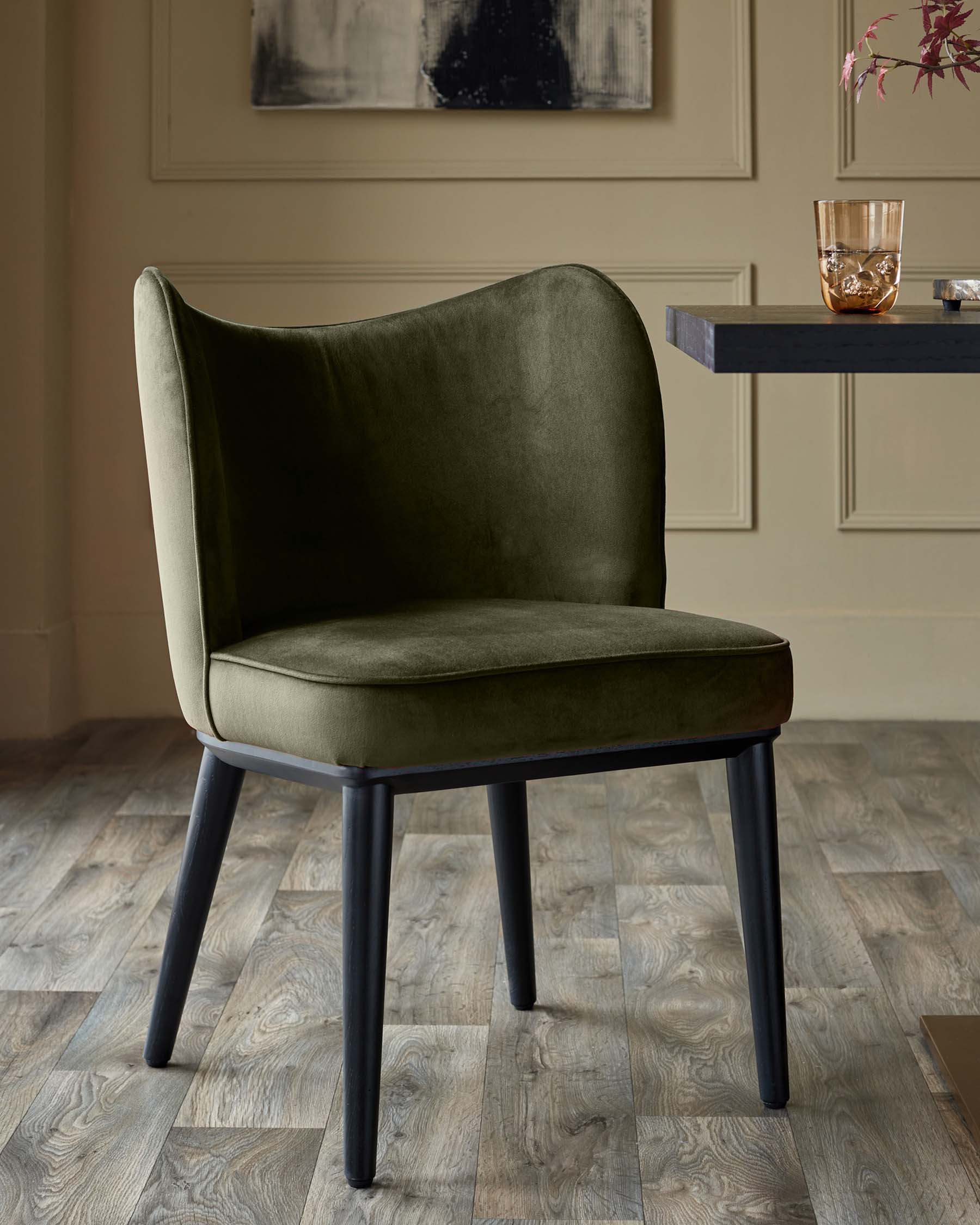A stylish olive velvet dining chair with dark, angled legs, set against a neutral backdrop.