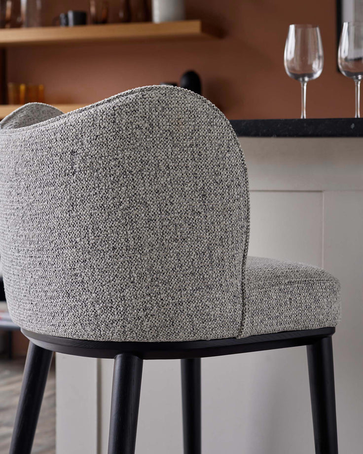 Close up of a stylish grey fabric bar stool with a curved back and dark wooden legs in a kitchen setting.