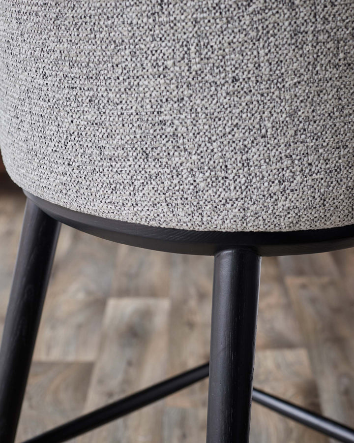 Close-up of a grey fabric stool with black wooden legs. Modern furniture design.