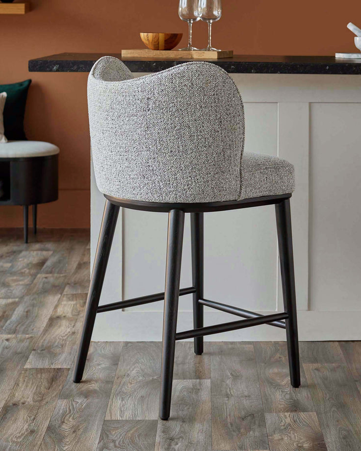 A grey upholstered bar stool with a dark wooden frame stands on a wooden floor. Minimalist design for the modern home.