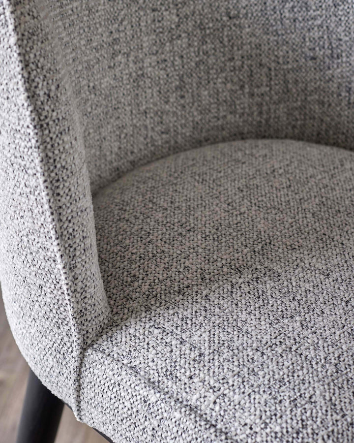 Close-up of a grey upholstered chair. The fabric has a textured, speckled pattern with light and dark fibres woven together.