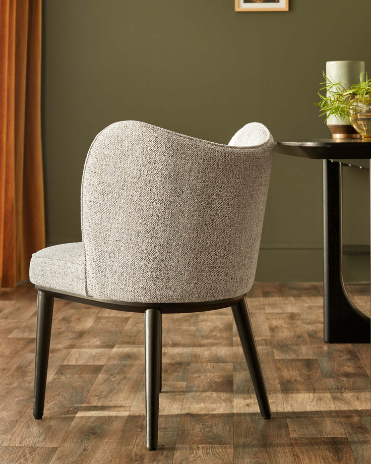 Upholstered dining chair in neutral fabric with dark wood legs next to a dark wood table with a vase.