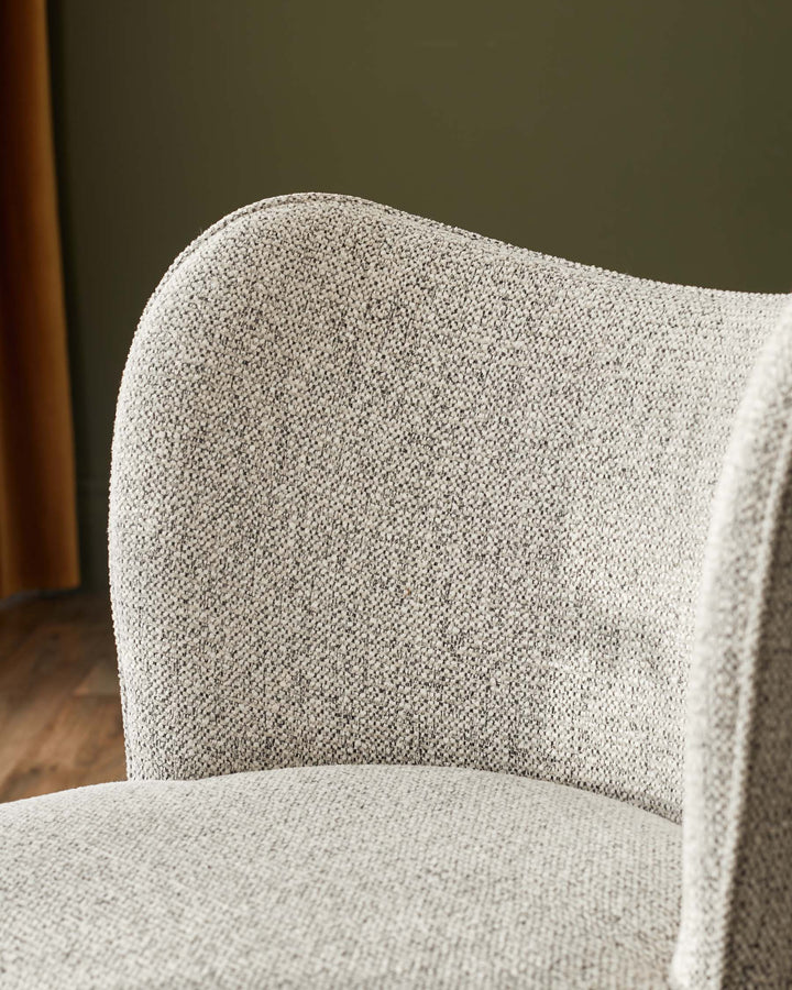 Close-up of a modern armchair with a textured, light grey fabric. Part of the seat, back and arm are in frame.