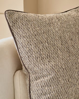 Fabian Large Natural Cushion with textured weave fabric and dark piping, displayed on cream upholstered furniture.