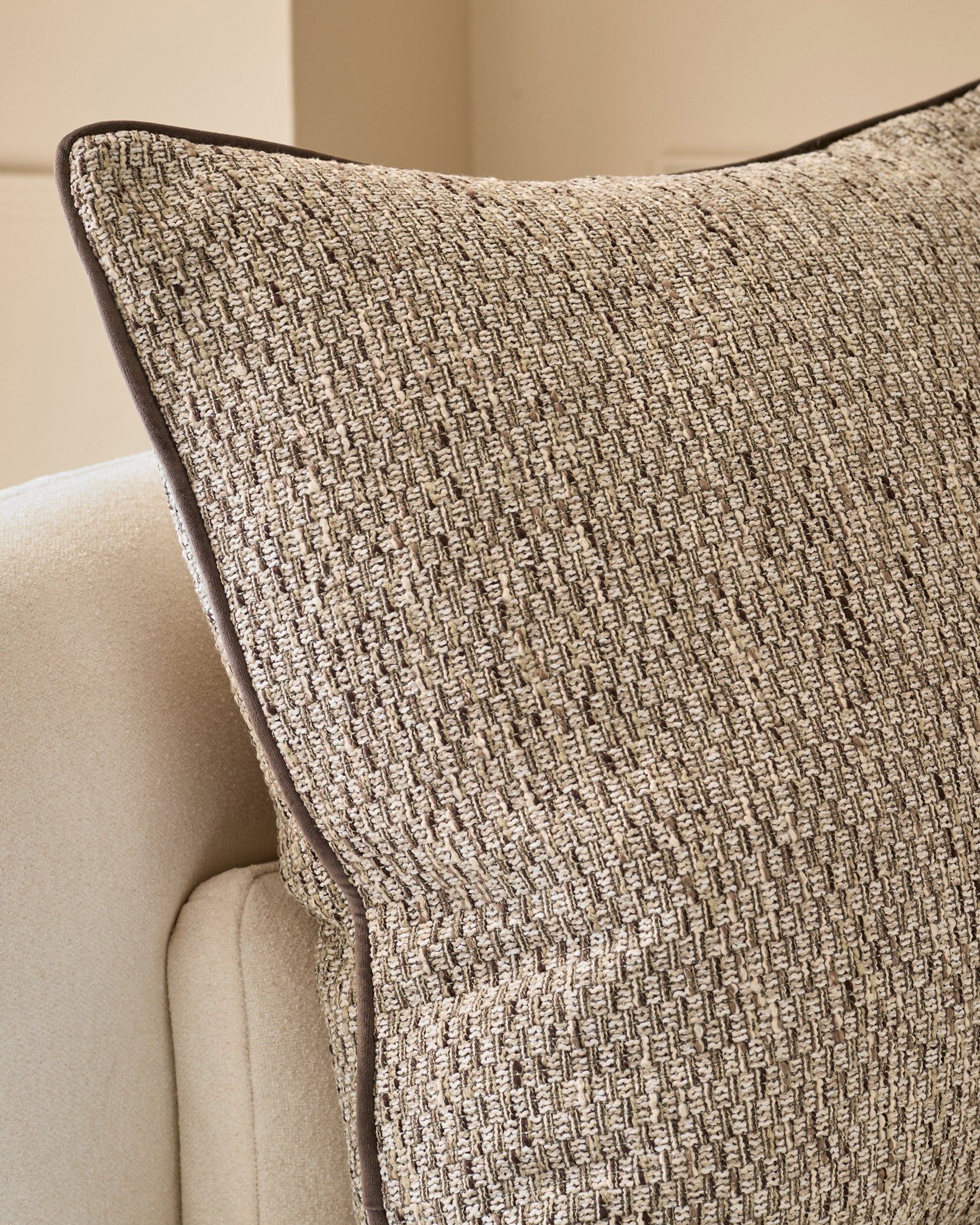 Fabian Large Natural Cushion with textured weave fabric and dark piping, displayed on cream upholstered furniture.