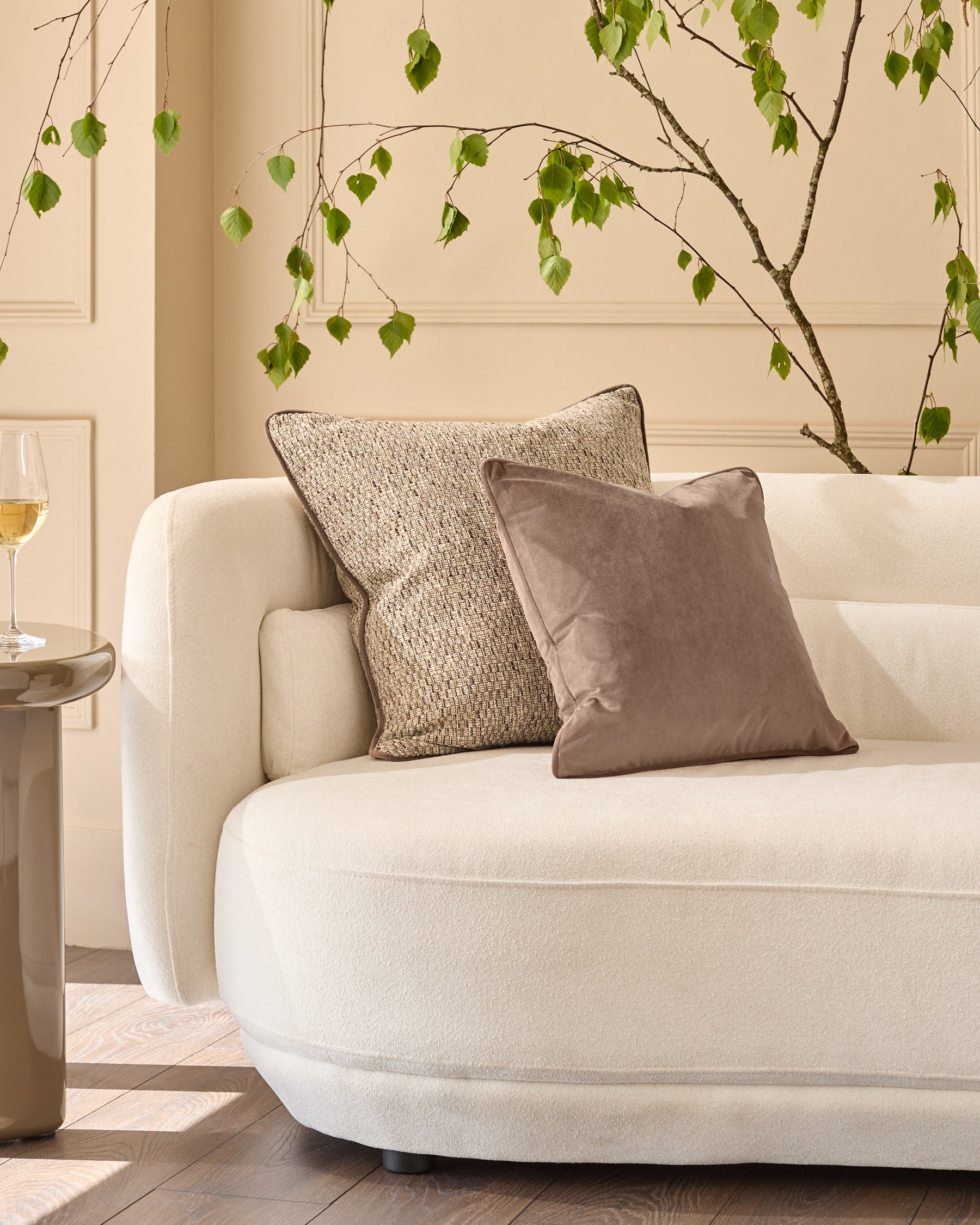 Large natural textured cushion displayed on a cream curved sofa with decorative styling.