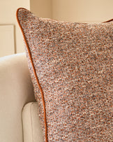 Rust-colored textured cushion with brown leather piping, displayed on a cream upholstered chair.