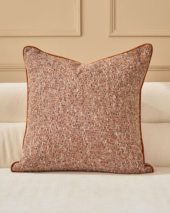 Fabian cushion in rust with textured weave, displayed on a cream sofa against a neutral wall with paneling.