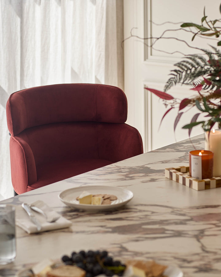 Felix bar stool in toffee red velvet, curved backrest design, shown at marble dining table with place settings and decor.