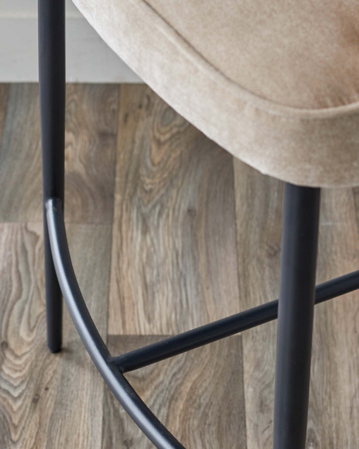 Close-up of a stool with a beige seat and dark metal legs, showcasing its modern design and sturdy construction.