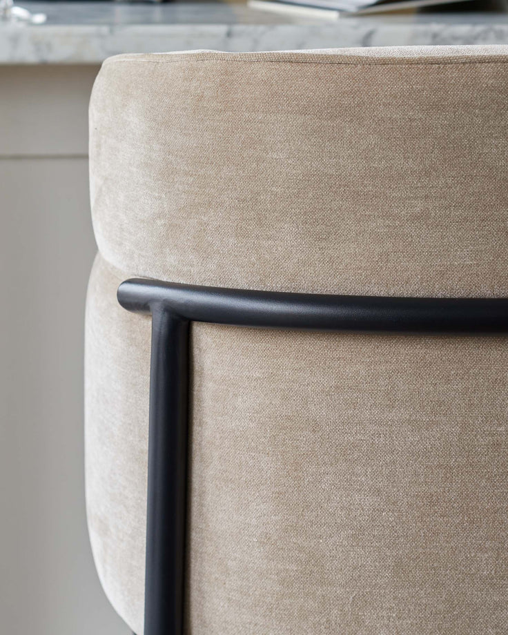 Close up of a tan, upholstered chair with black metal frame. The chair has a textured fabric and a modern, minimalist design.