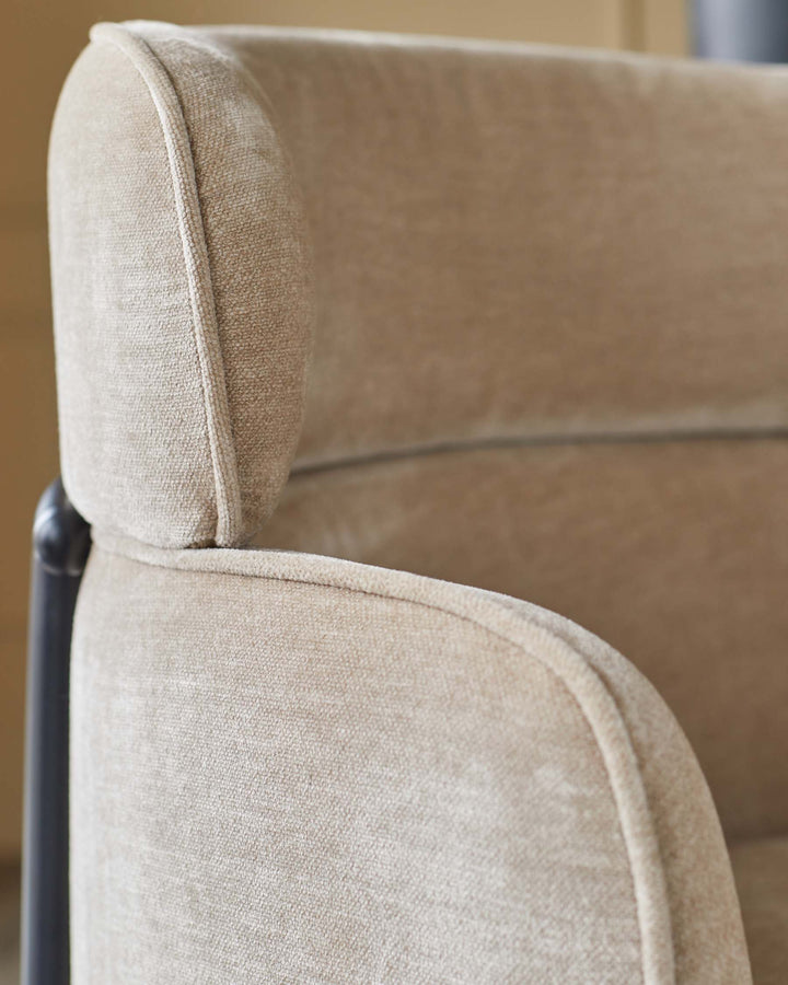 Close-up of a beige armchair with a curved armrest and a black metal frame, showcasing its texture and design.