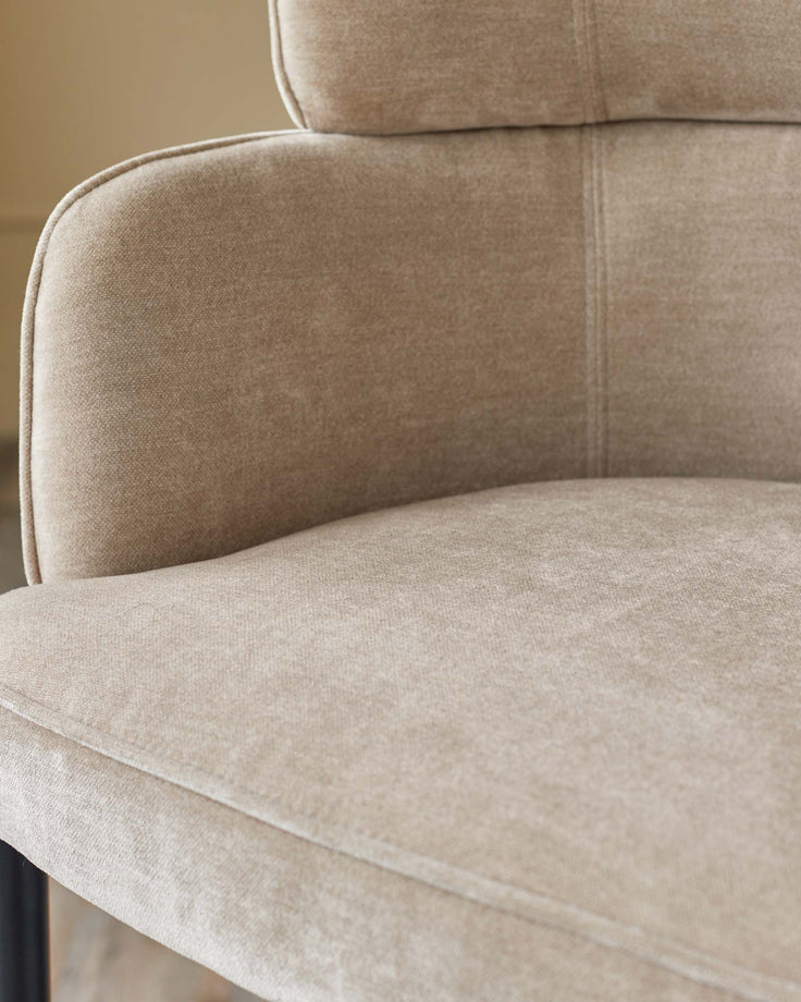 Close-up of a beige fabric chair with a curved back and seat, showing detailed texture and stitching.