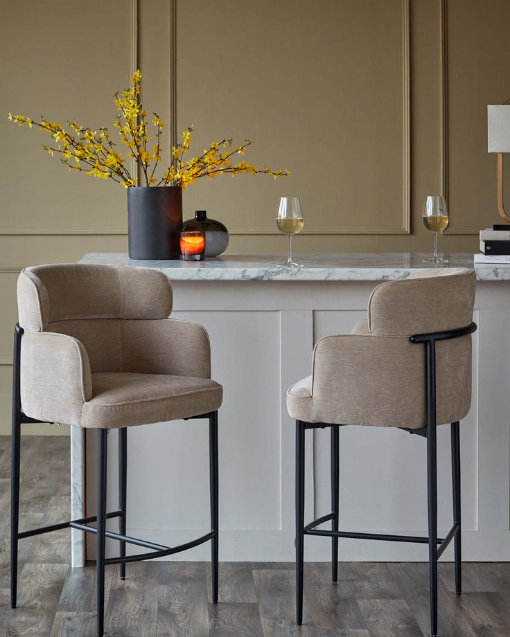Two upholstered bar stools with dark metal legs stand beside a breakfast bar with a marble countertop.