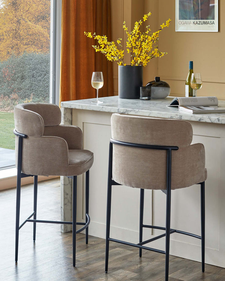 Two upholstered bar stools with a curved backrest and black metal legs are placed near a kitchen island.