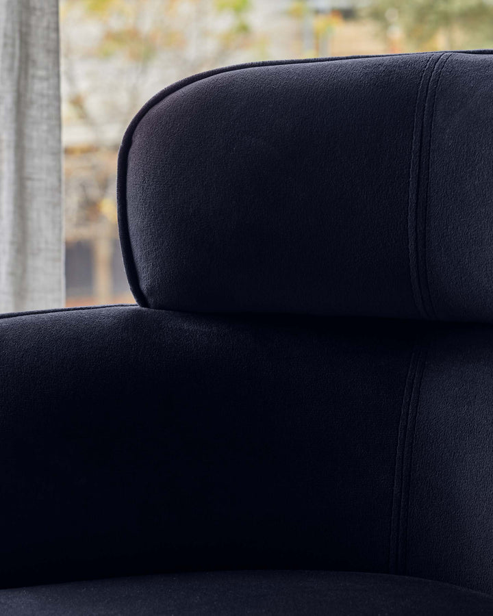 Close-up of a plush, navy blue chair with a rounded backrest and subtle seam detailing. Soft, inviting texture.