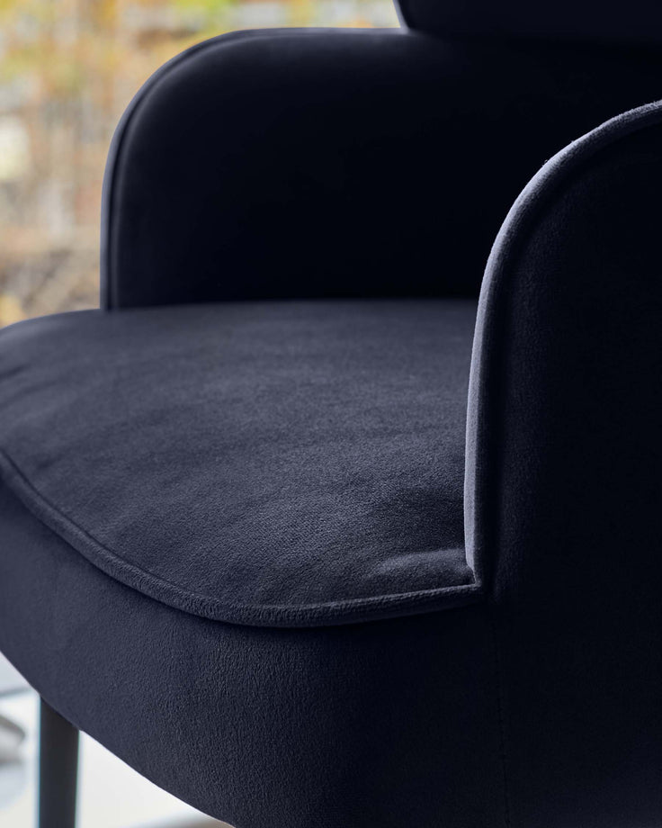 Close-up of a stylish, dark-upholstered chair with curved armrests, showcasing its plush texture and modern design.