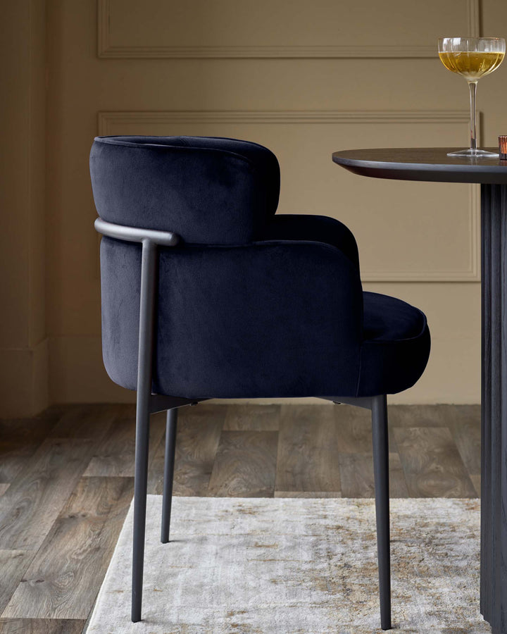 A deep blue upholstered chair with metal frame at a small table with a drink in a champagne coupe.