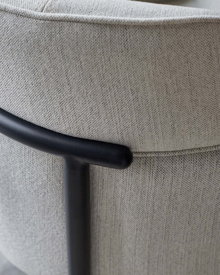 Close-up of a fabric chair with a sleek, black metal armrest, showcasing modern design and textile detail.