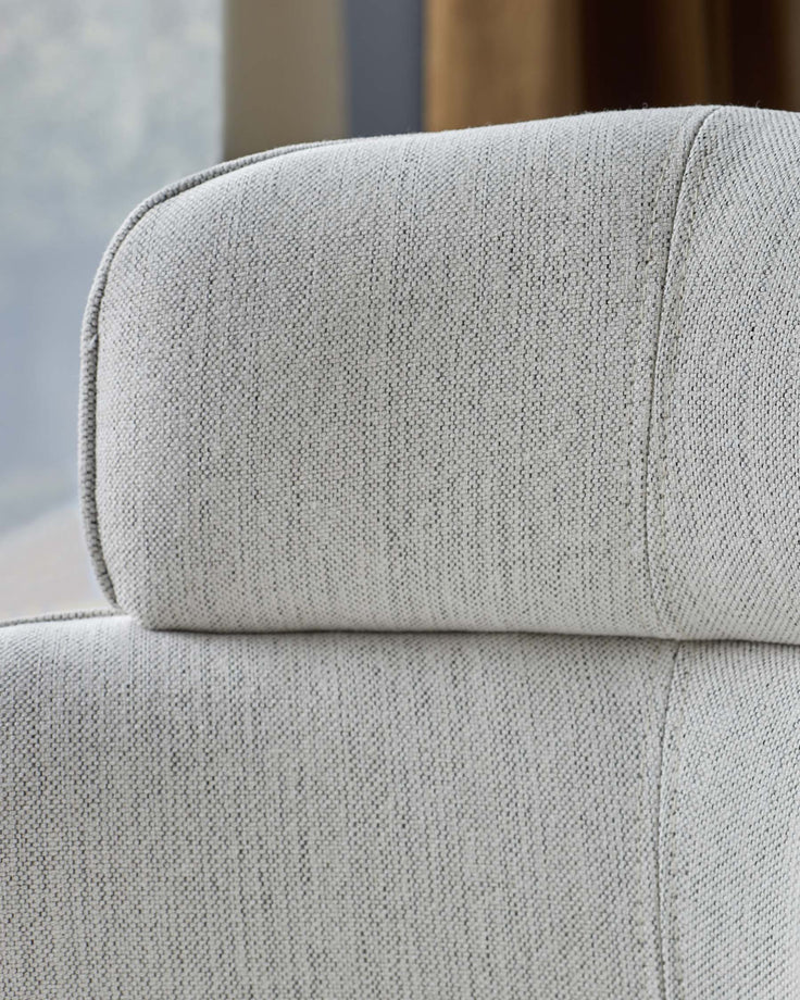 Close-up of a light grey, textured fabric sofa back and headrest. Modern, comfortable design.