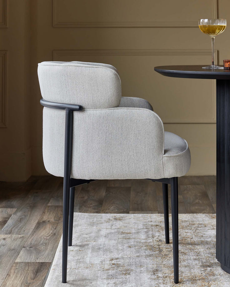 A grey upholstered chair with black legs, situated beside a table with a drink on it.