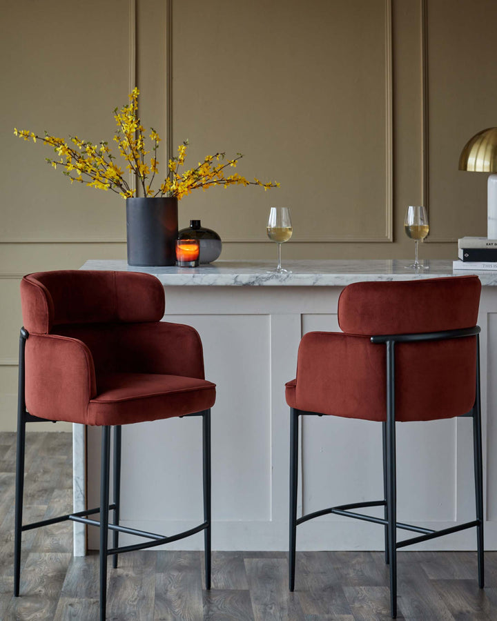 Two rust coloured velvet bar stools with black metal frames, in front of a bar with flowers and drinks.