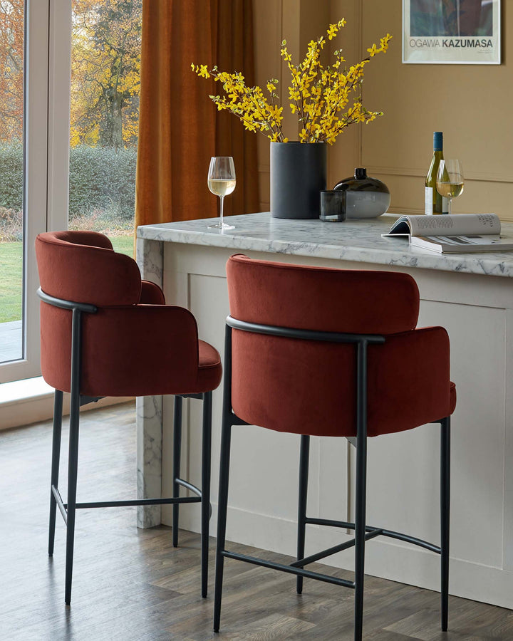 Two stylish rust-coloured velvet bar stools with black metal frames sit at a marble-topped kitchen island.