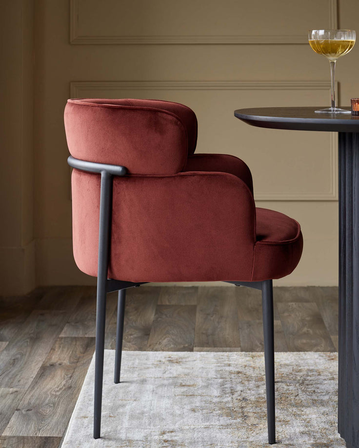 A plush velvet dining chair with a black metal frame, complemented by a sleek round table.